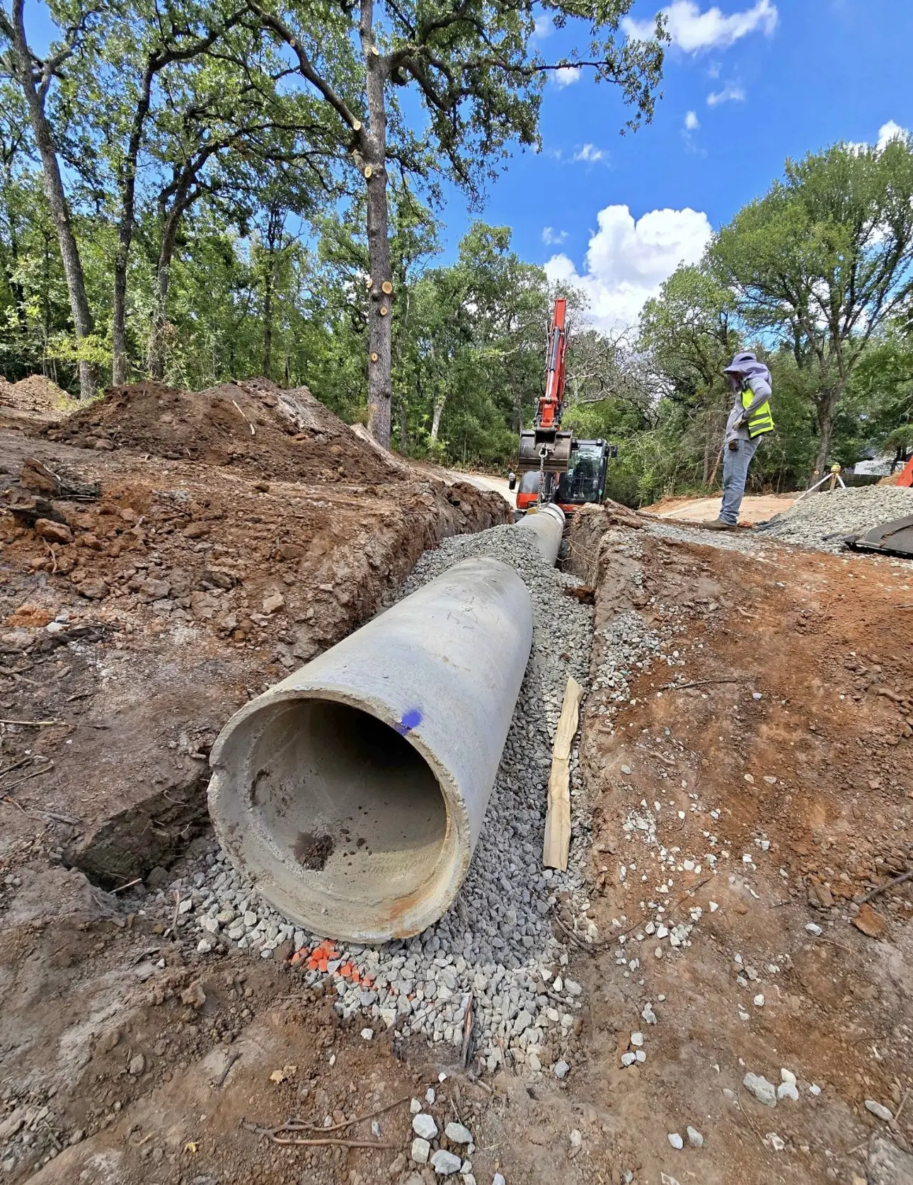 Large concrete pipeline being installed in a trench at a construction site.