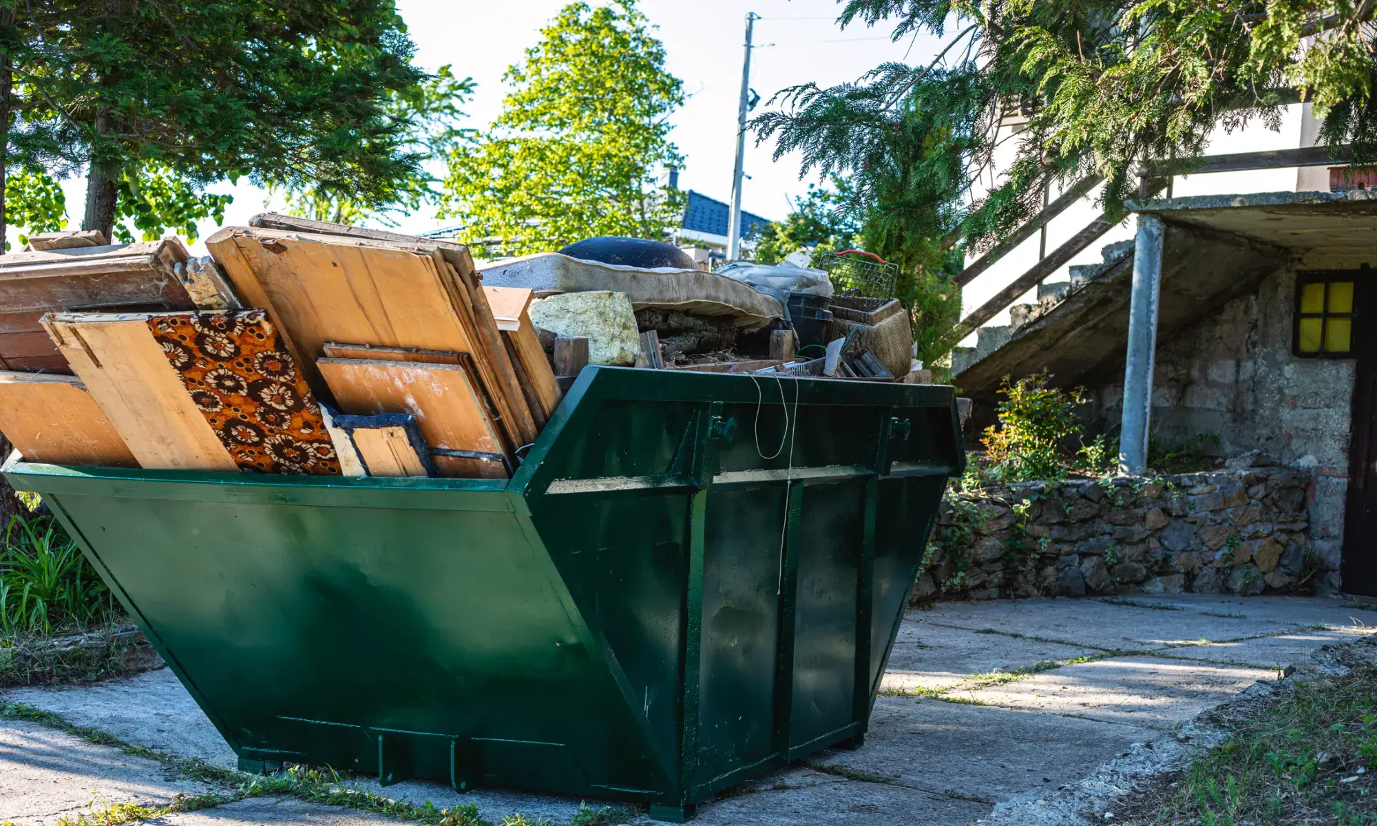 Green dumpster filled with wooden debris outside.