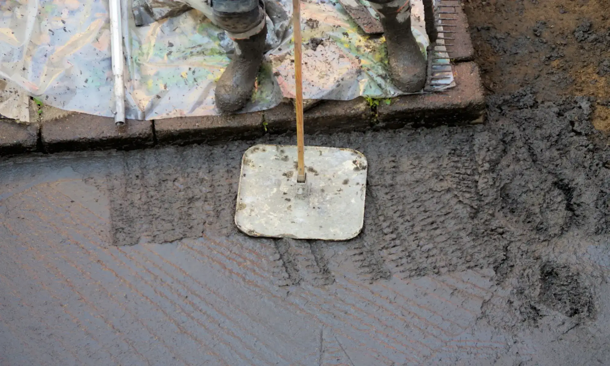 Worker smoothing wet concrete with tool.