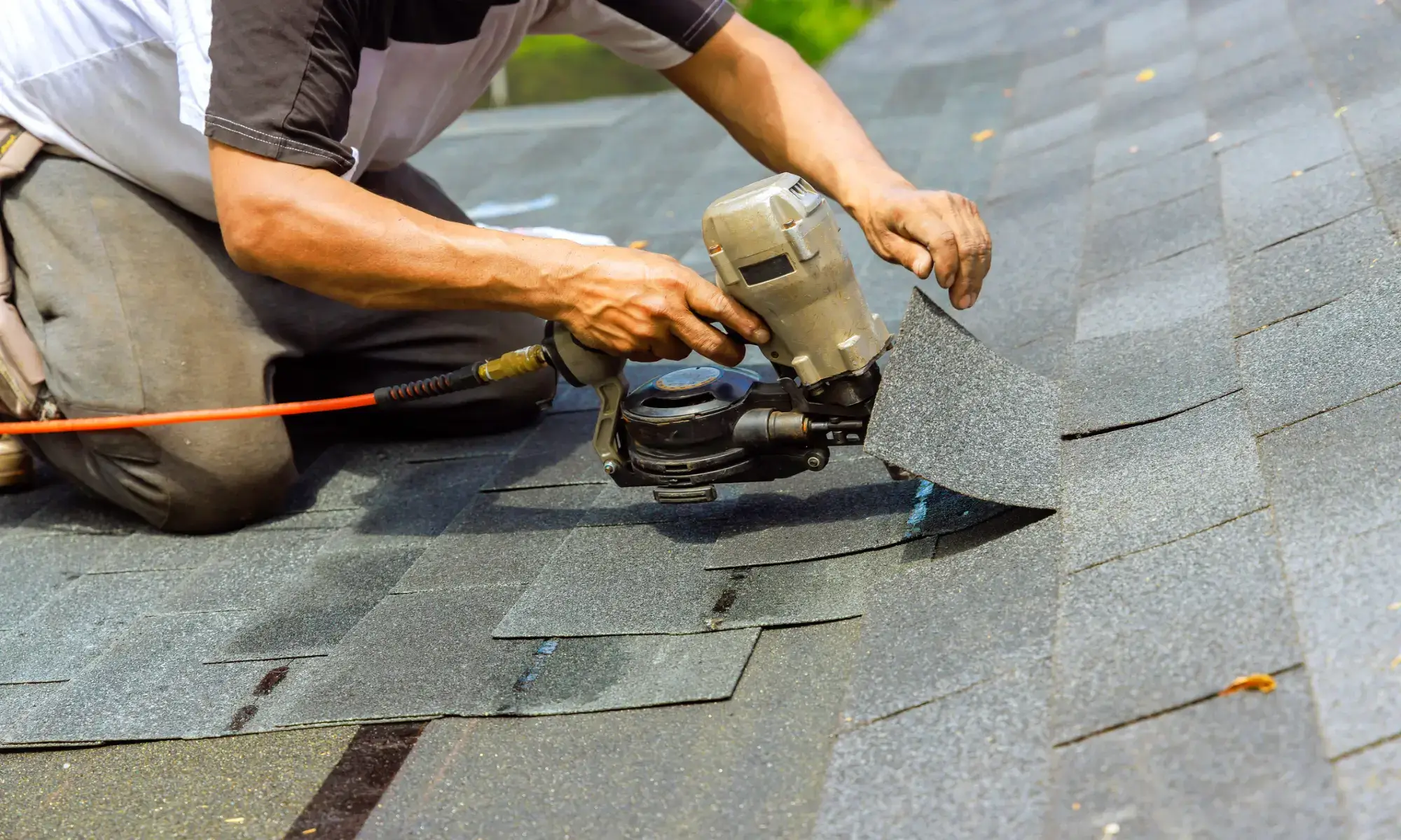 Worker using nail gun on roof shingles.