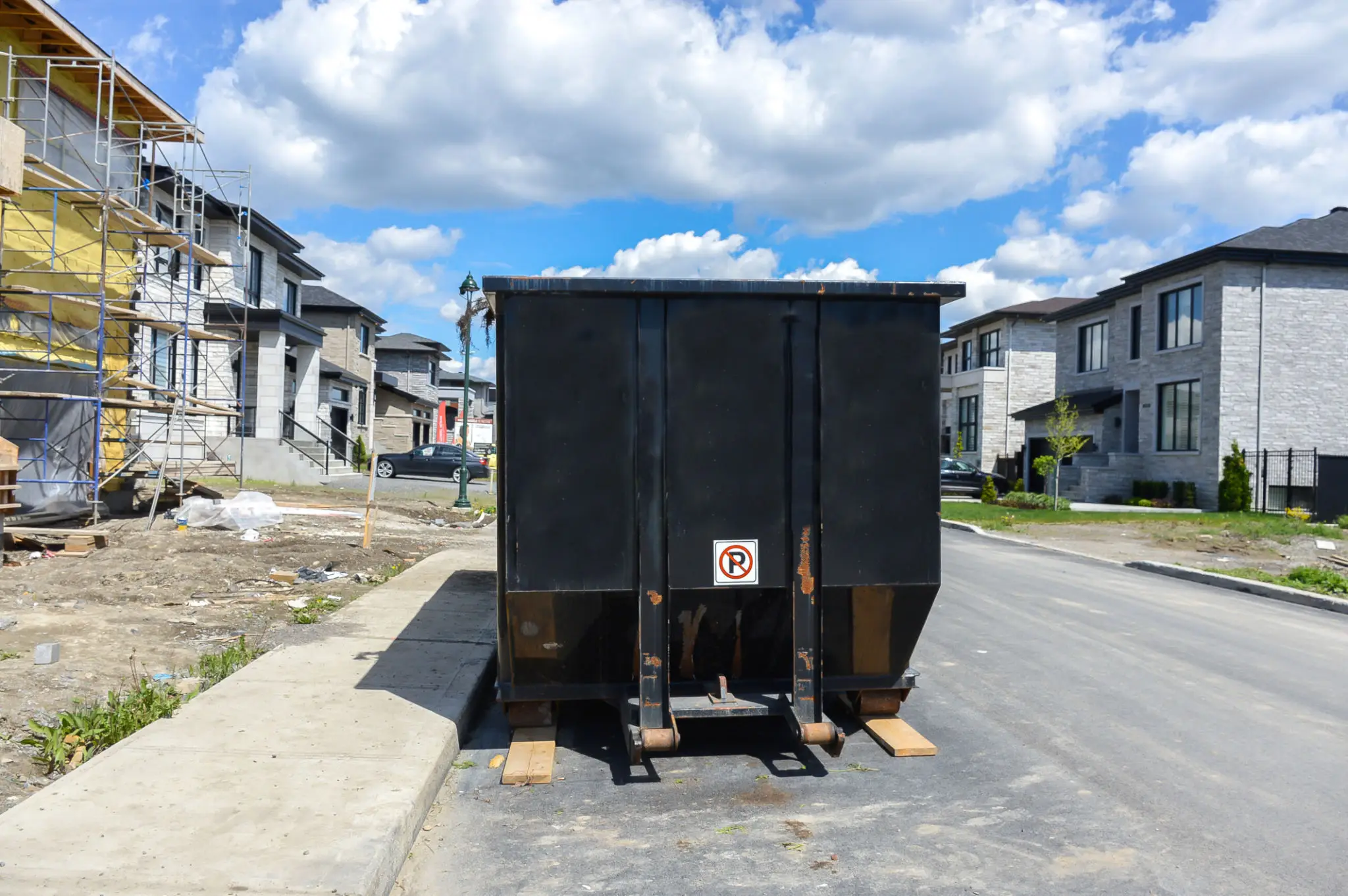 A large black dumpster on a residential street.