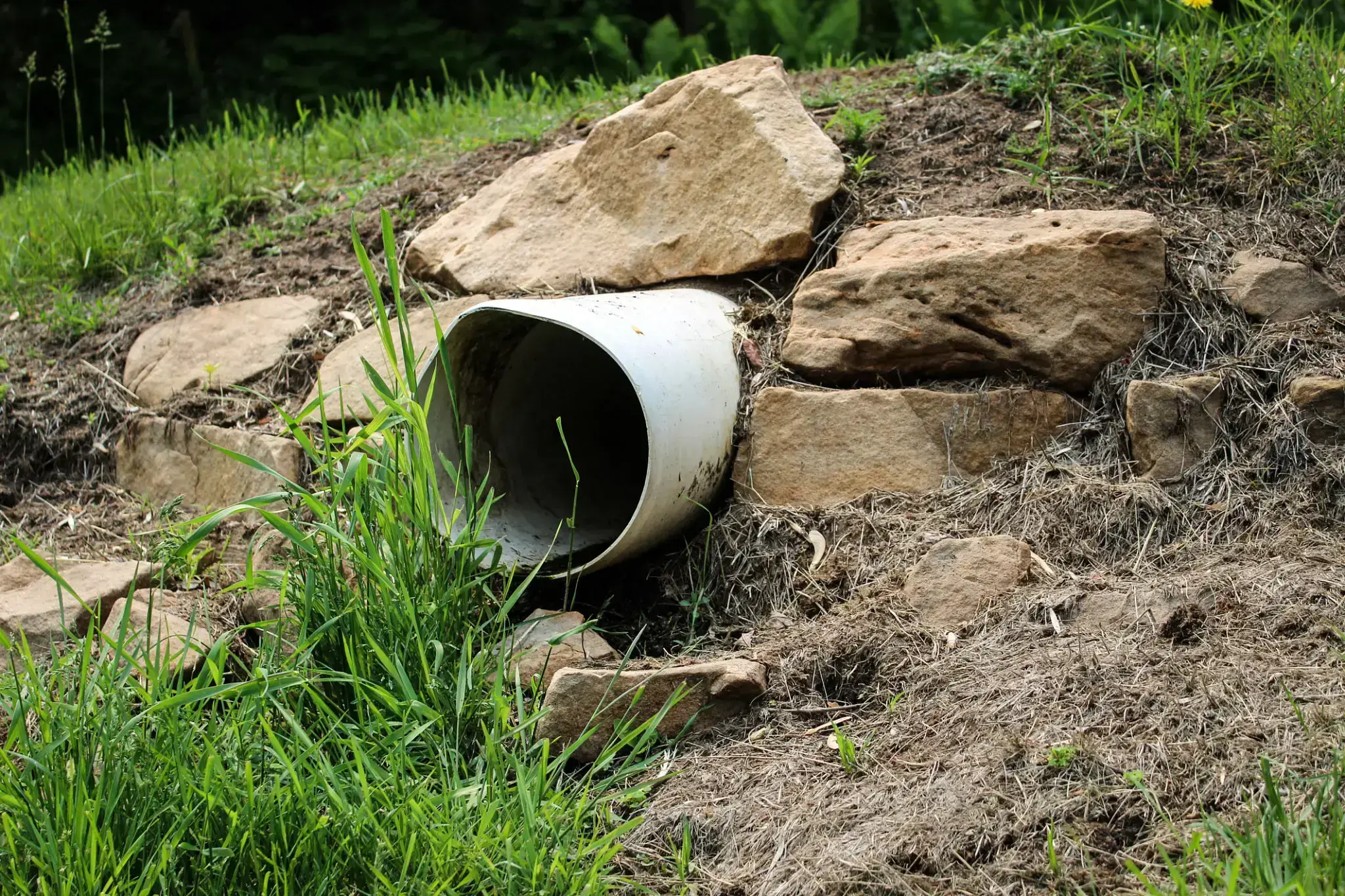 A drainage pipe embedded in a grassy and rocky slope.