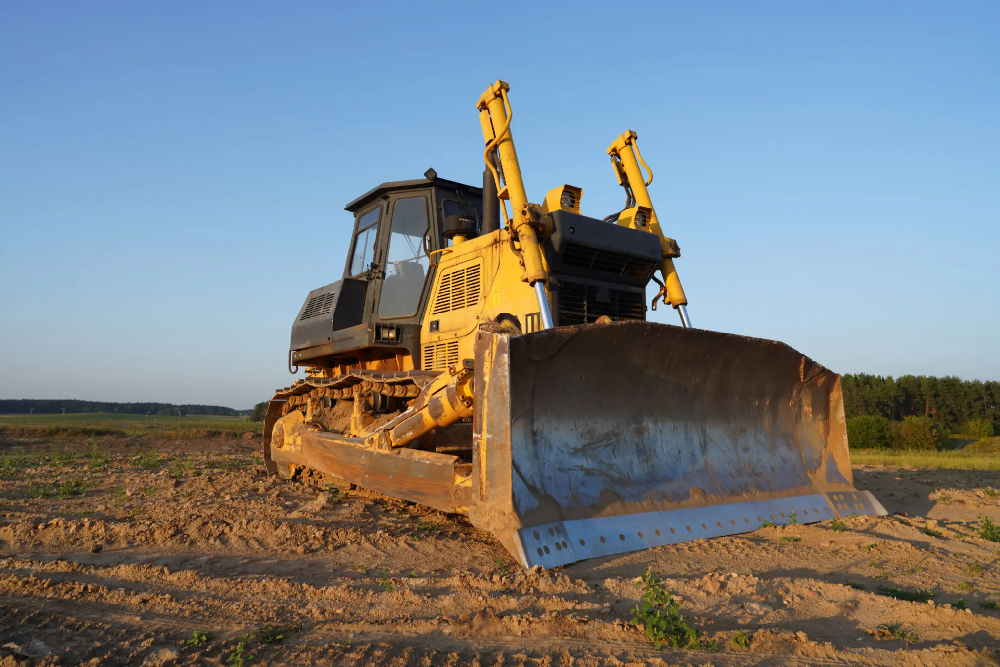 A yellow bulldozer on a dirt field under a clear blue sky.