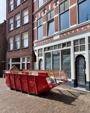 A large red dumpster placed on a street near brick buildings.