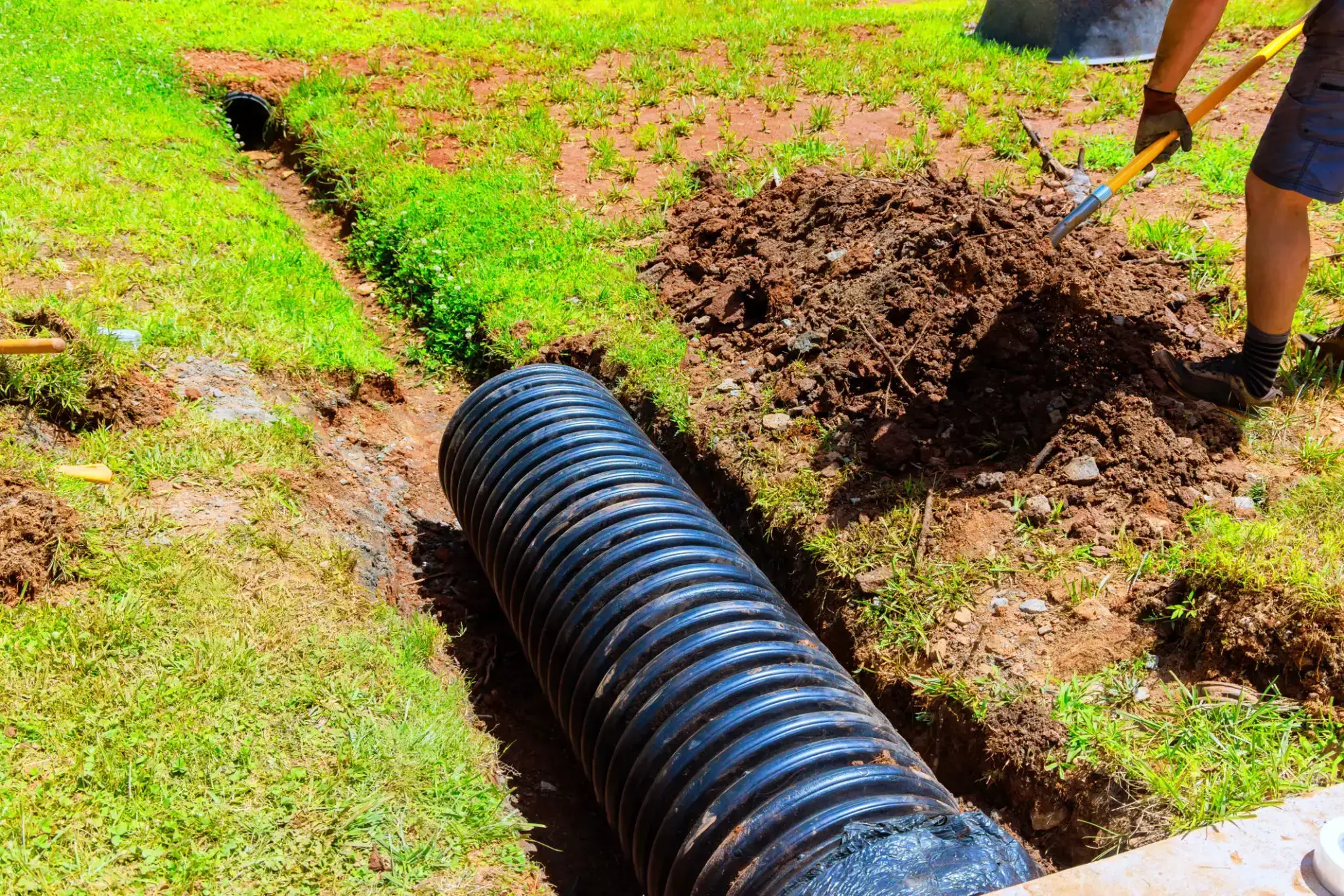Black corrugated drainage pipe installed in a grassy area with soil mound.